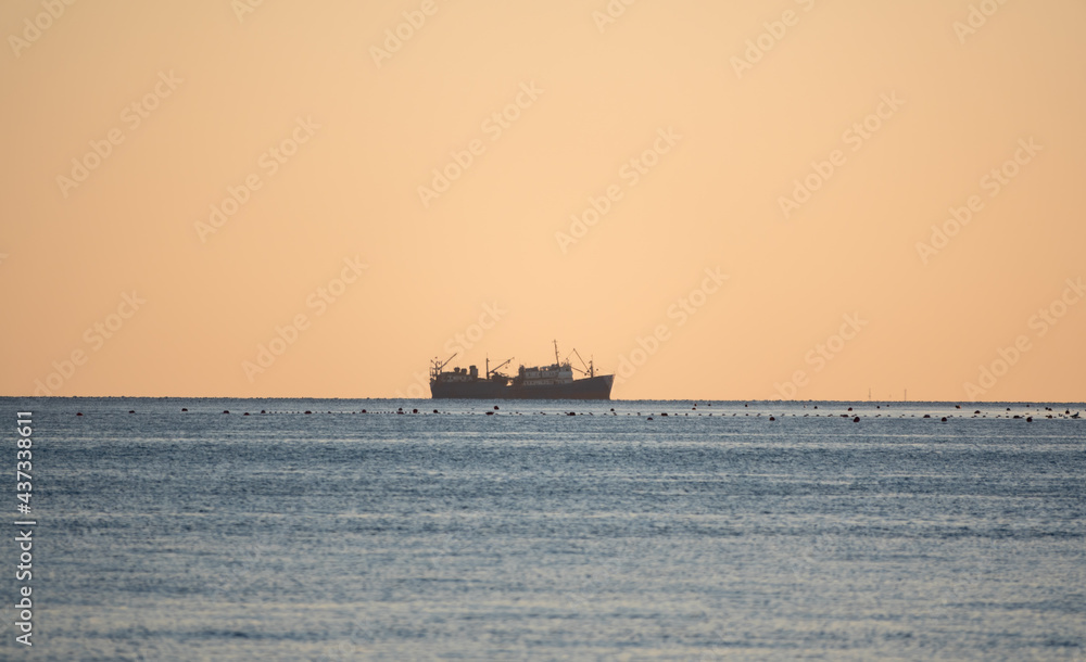 Calm blue sea with the silhouette of a large ship on the horizon