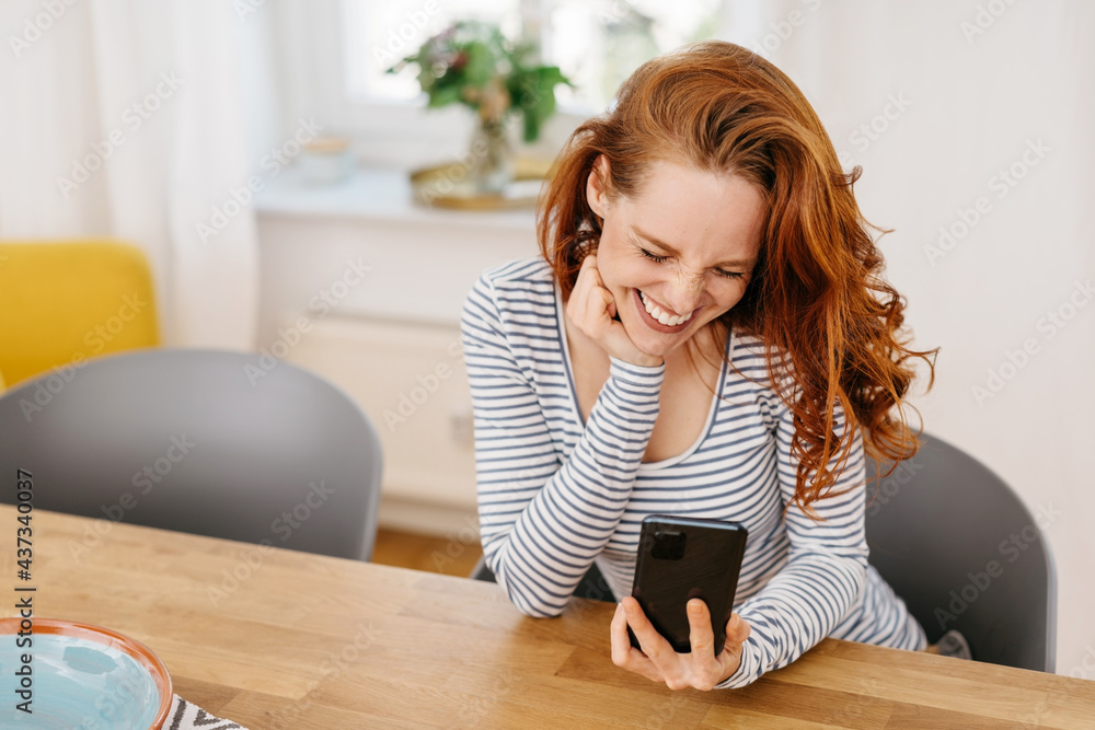 Laughing vivacious young woman enjoying a joke on her mobile Laughing vivacious young woman enjoying a joke on her mobile
