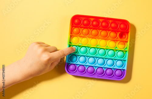 A child s hand presses on pop it toy silicone on a yellow background. Anti-stress toy  a trend in children s toys. 