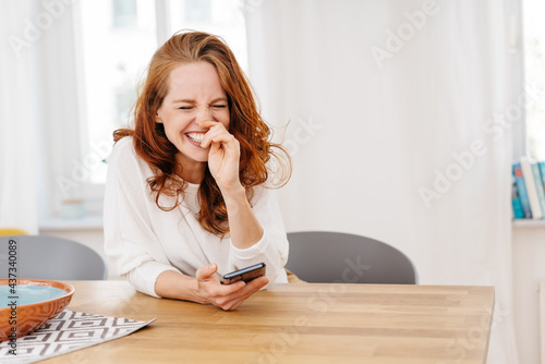 Happy young redhead woman sitting sniggering to herself