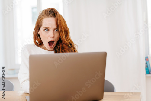 Billede på lærred Young woman staring wide eyed at her laptop computer
