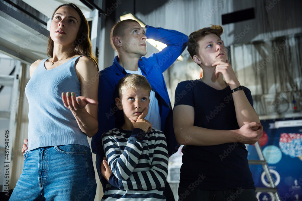 Fototapeta premium Two interested teen boys with their parents trying to get out of closed space of escape room stylized under abandoned nuclear bunker, contemplating solving conundrums..
