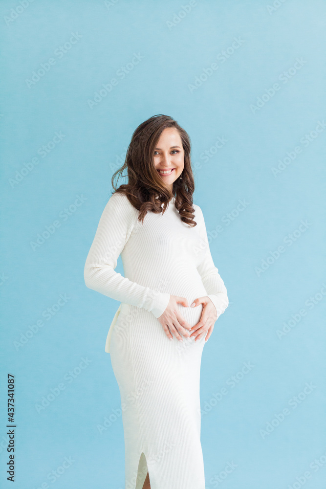 Beautiful pregnant woman making heart on her belly on blue background Beautiful pregnant woman making heart on her belly on blue background
