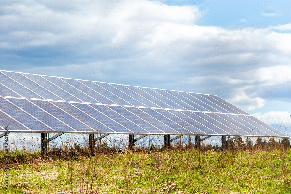 Solar panels in a field.line of solar electric generation panels on rural meadow.Cloudy evening sky background. Solar panels in a field.line of solar electric generation panels on rural meadow.Cloudy evening sky background.
