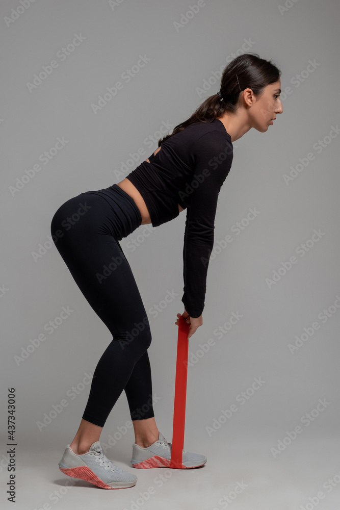 Woman performing resistance band deadlifts on grey background Woman performing resistance band deadlifts on grey background