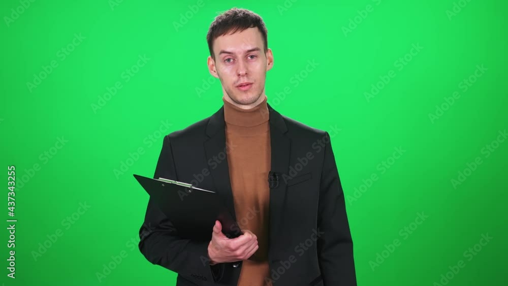 Man reporter in suit looks into the camera and speaks in lavalier microphone, holding a folder of documents in his hands, man on a green background, a template for TV news agencies, journalist at work Man reporter in suit looks into the camera and speaks in lavalier microphone, holding a folder of documents in his hands, man on a green background, a template for TV news agencies, journalist at work
