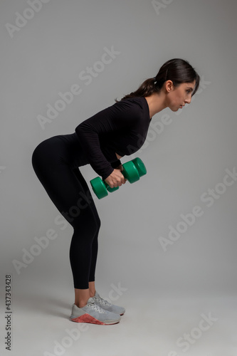 Athletic girl doing dumbbell triceps kickback on grey background photo