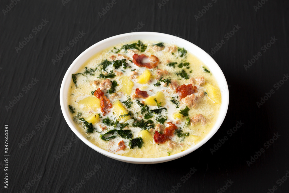 Homemade Zuppa Toscana with Kale and Bread in a white bowl on a black background, side view. Homemade Zuppa Toscana with Kale and Bread in a white bowl on a black background, side view.