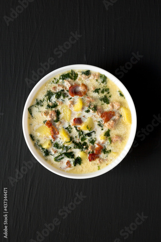 Homemade Zuppa Toscana with Kale and Bread in a white bowl on a black background, top view. Overhead, from above, flat lay.