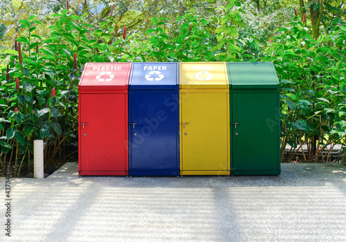 Simple metal recycling bins in bright colours for trash sorting. For mockup purpose. Plants in background