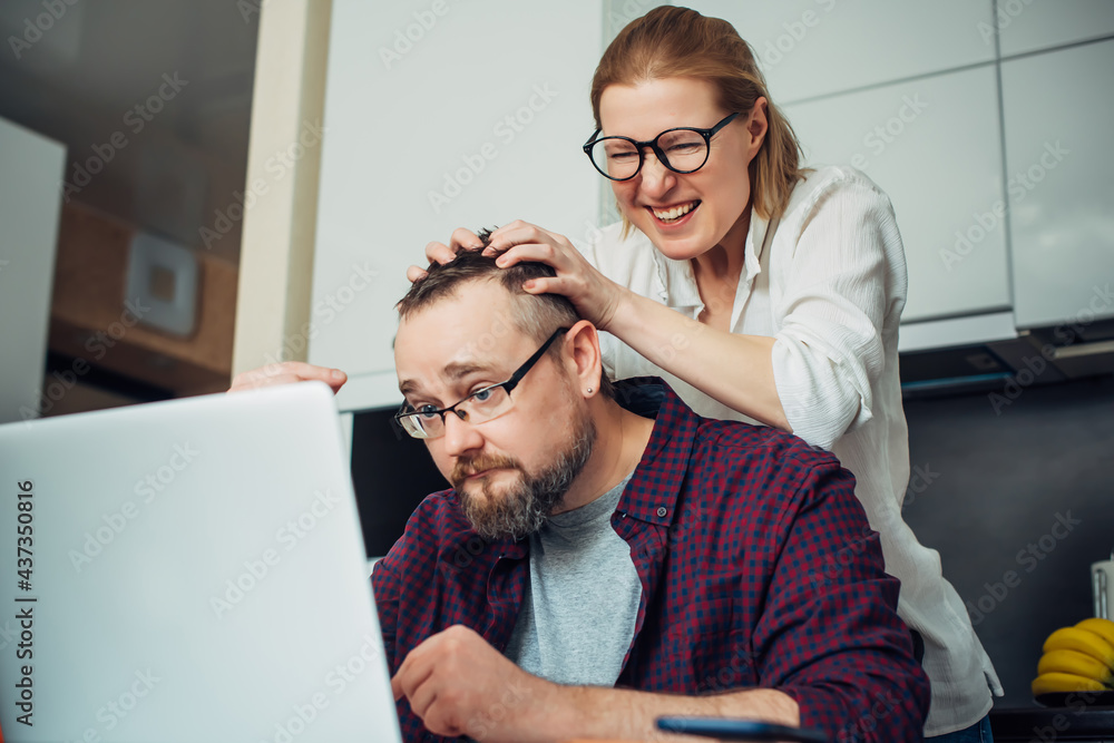 Bearded man and woman with eyeglasses using laptop in the home interior, communicate with friends online, laugh and grimace. Bearded man and woman with eyeglasses using laptop in the home interior, communicate with friends online, laugh and grimace.