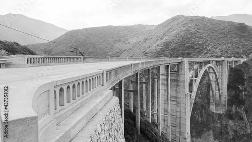 The famous Bixby Creek Brigde, Big Sur, California, USA, running closer to the hills. White overcasted sky. Monochromatic.