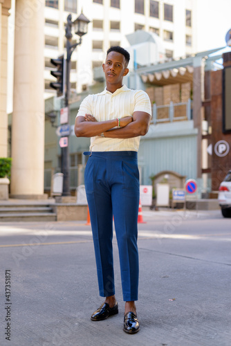 Full length shot of young African businessman outdoors in city streets looking at camera with arms crossed