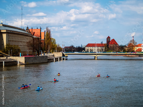 People on kayaks sailing by the river in a city.