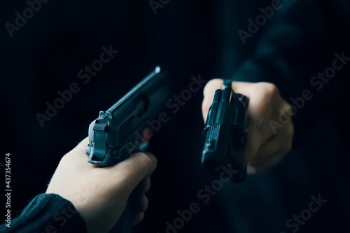 Two men's hands with weapons pointed at each other. Shootout with firearms of two criminals on dark background. Killer with gun. Detective with a revolver.