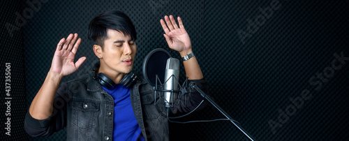 Fotografija Young asian man dance, swaying, and lifting his arms rhythmically while singing in front of black soundproofing wall