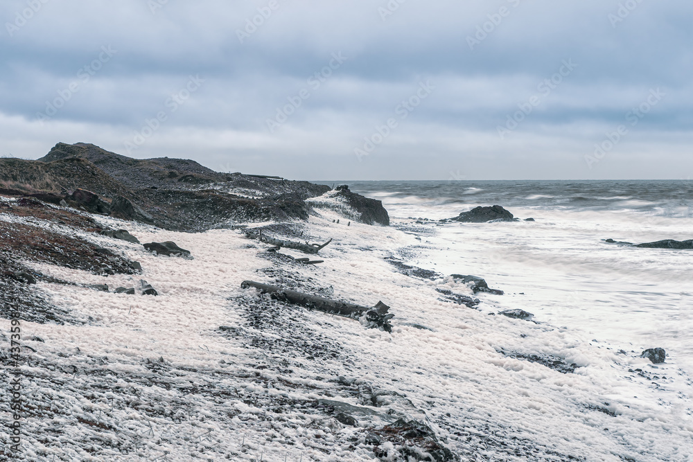 Stormy ocean. Waves with white foam roll on the rocky shore.