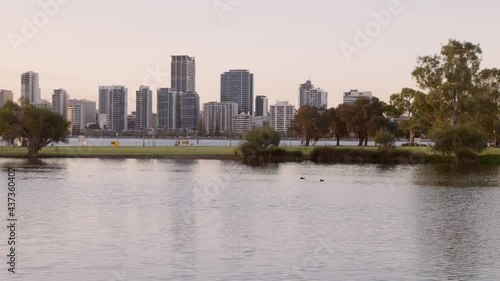 Moving view across pond in foreground. Pelicans rest. Walkers, bike riders by Swan Rriver. Perth City in background. photo