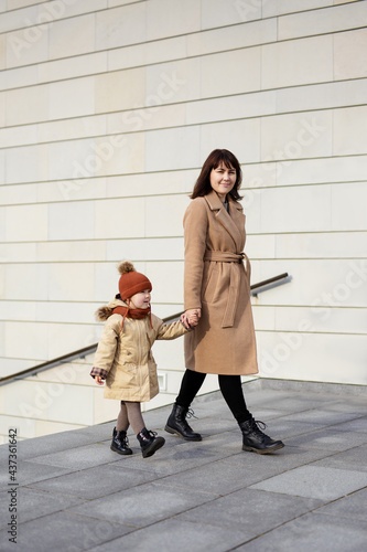 family, motherhood, love and care concept - happy mother and her little daughter walking hand in hand in warm clothes