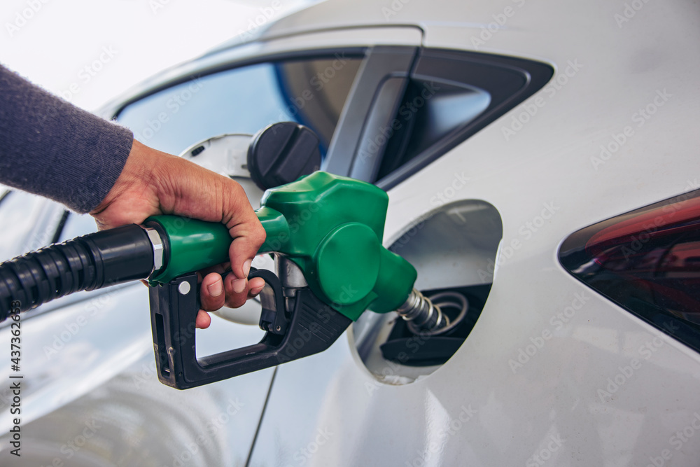 Man Handle pumping gasoline fuel nozzle to refuel. Vehicle fueling facility at petrol station. White car at gas station being filled with fuel. Transportation and ownership concept Man Handle pumping gasoline fuel nozzle to refuel. Vehicle fueling facility at petrol station. White car at gas station being filled with fuel. Transportation and ownership concept
