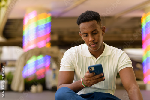 Portrait of young African businessman wearing casual clothes and using mobile phone while sitting