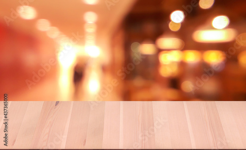 Close up wooden table top in front of abstract bokeh blur background, .hallway in shopping mall, and ice cream shop on right side in shopping mall.
