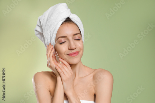 Beautiful young woman with hair wrapped in towel after washing on light green background