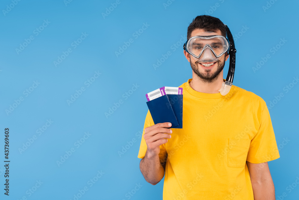 Positive man in swimming goggles holding air tickets and passports isolated on blue Positive man in swimming goggles holding air tickets and passports isolated on blue