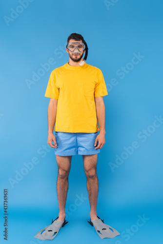 Man in shimming goggles and flippers looking at camera on blue background