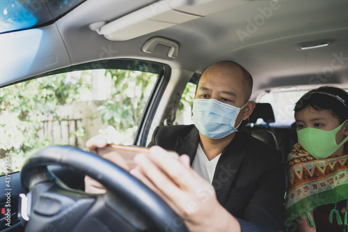 young man sitting in car with daughter and wearing healthy face mask. © tienuskin