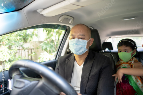 Young father sitting in car with daughter wearing healthy face mask. © tienuskin