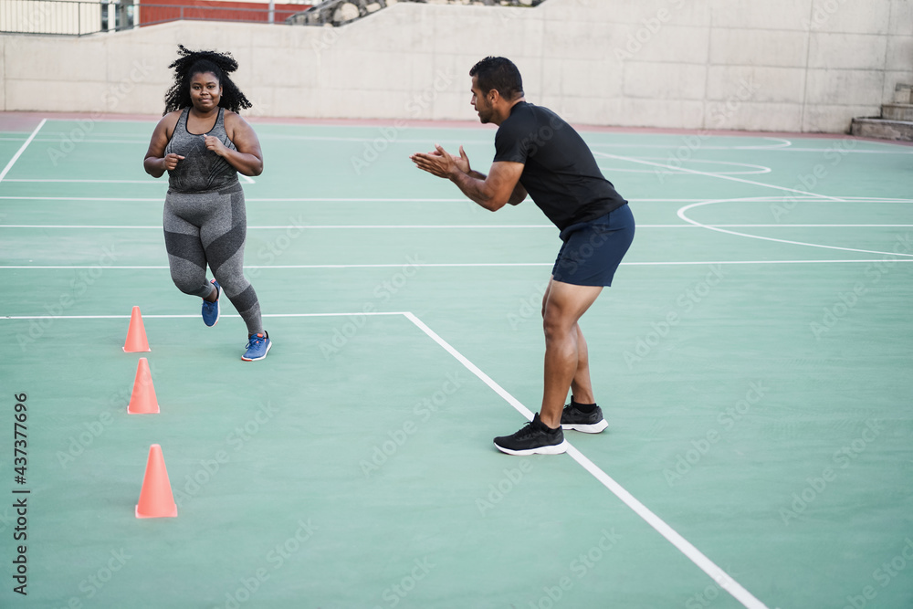 Plus size woman and personal trainer doing speed and agility cone drills workout session outdoor - Focus on girl face