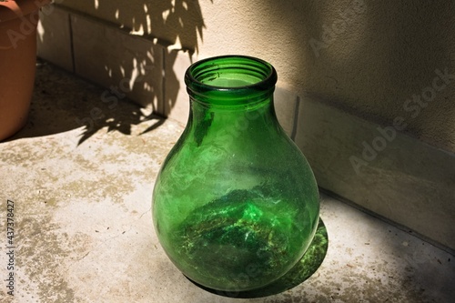 An empty green blown glass vase resting on the ground in the garden (Marche, Italy, Europe)