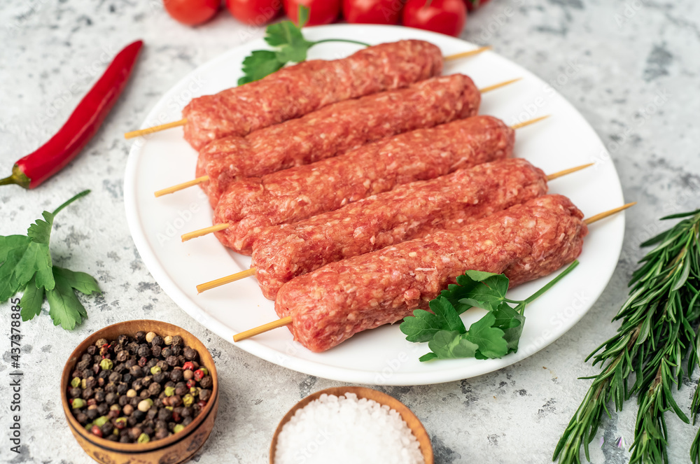 raw Lula kebab on skewers with spices on a white plate on a light stone background raw Lula kebab on skewers with spices on a white plate on a light stone background