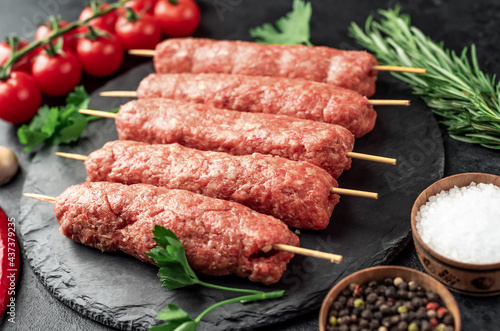 raw Lula kebab on skewers with spices on a stone background