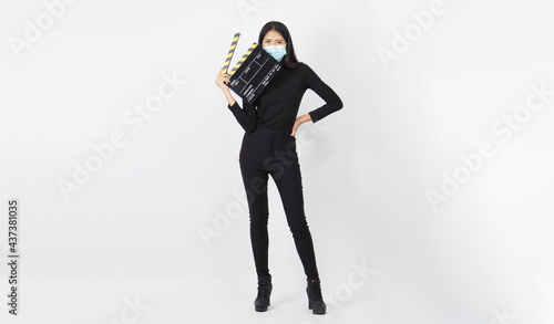 Asian young woman wear face mask or medical mask and hand's hold black clapper board or movie slate use in video production ,film, cinema industry on white background. Full-length photo