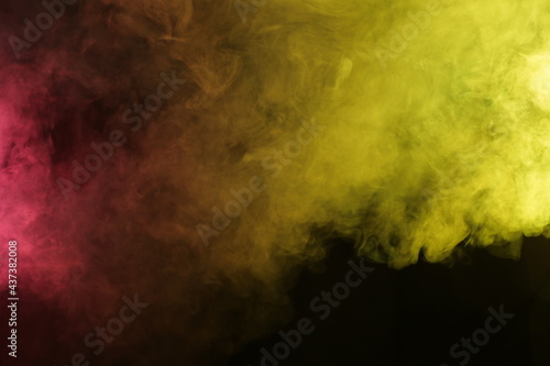 Artificial magic smoke in red-yellow light on black background