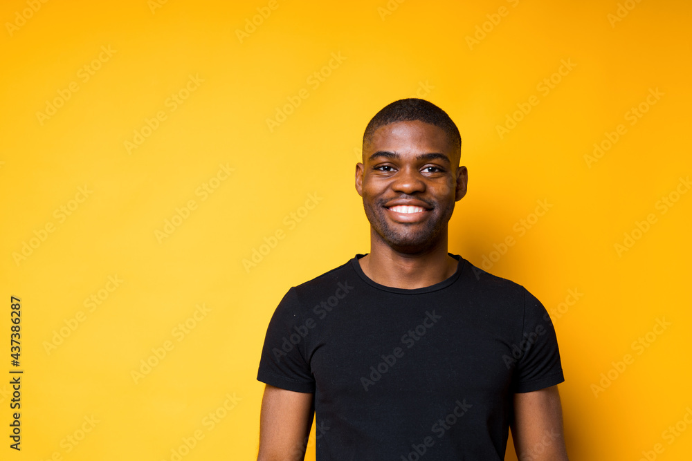Portrait of a happy African American man in a black t-shirt smiling at the camera. Isolated on yellow background Portrait of a happy African American man in a black t-shirt smiling at the camera. Isolated on yellow background