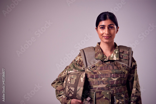 Studio Portrait Of Smiling Young Female Soldier In Military Uniform Against Plain Background