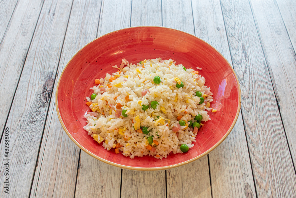 Three delicious rice dishes typical of a Chinese restaurant with fried egg filaments, carrot pieces, ham and peas in a red deep plate Three delicious rice dishes typical of a Chinese restaurant with fried egg filaments, carrot pieces, ham and peas in a red deep plate