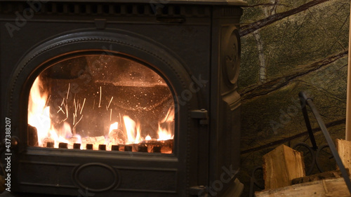 Selective focus burning fire in cast-iron potbelly stove of retro style interior. Blurred flame in antique fireplace. Norwegian style craft cast iron stove