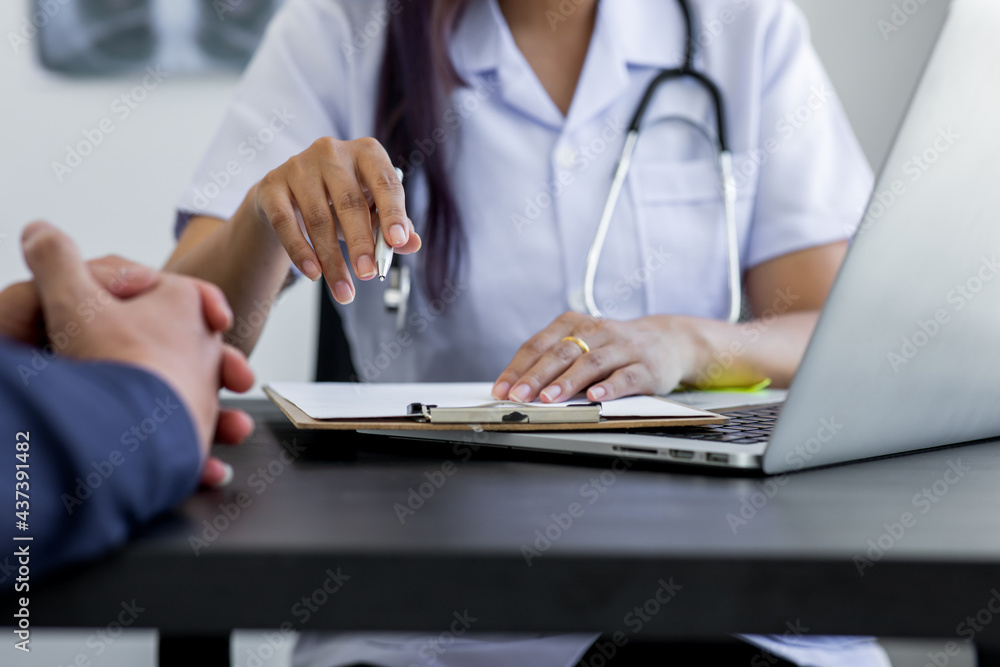 Fototapeta premium Close up of doctor and patient taking, doctor working with laptop computer and writing on paperwork. Hospital background.