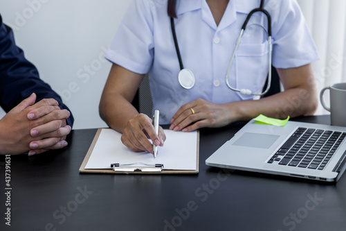 Close up of doctor  and patient taking, doctor working with laptop computer and writing on paperwork. Hospital background. photo