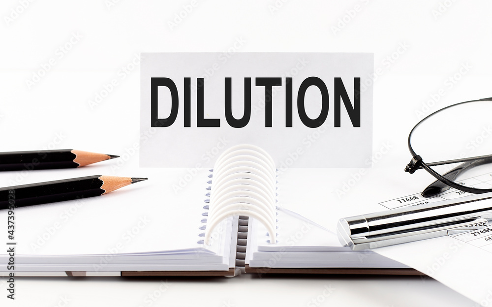 Text DILUTION on paper card,pen, pencils, glasses,financial documentation on table - business concept Text DILUTION on paper card,pen, pencils, glasses,financial documentation on table - business concept