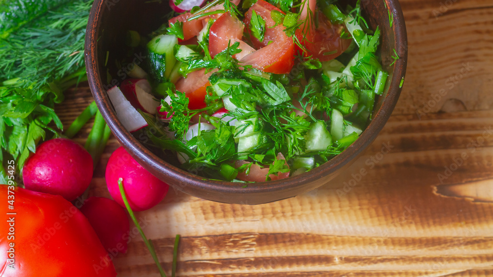 Salad of fresh spring vegetables in a clay bowl. Salad ingredients radish, tomato, cucumber, onion, parsley, dill on a brown wooden table