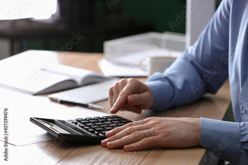 Man using calculator at wooden table indoors, closeup