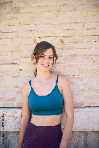 Fit girl posing looking to the camera before going out to exercise in the city. Leaning against a brick wall. © nicuervo
