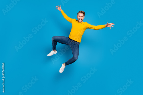 Full length body size of young guy jumping up cheerful laughing careless playful isolated bright blue color background © deagreez