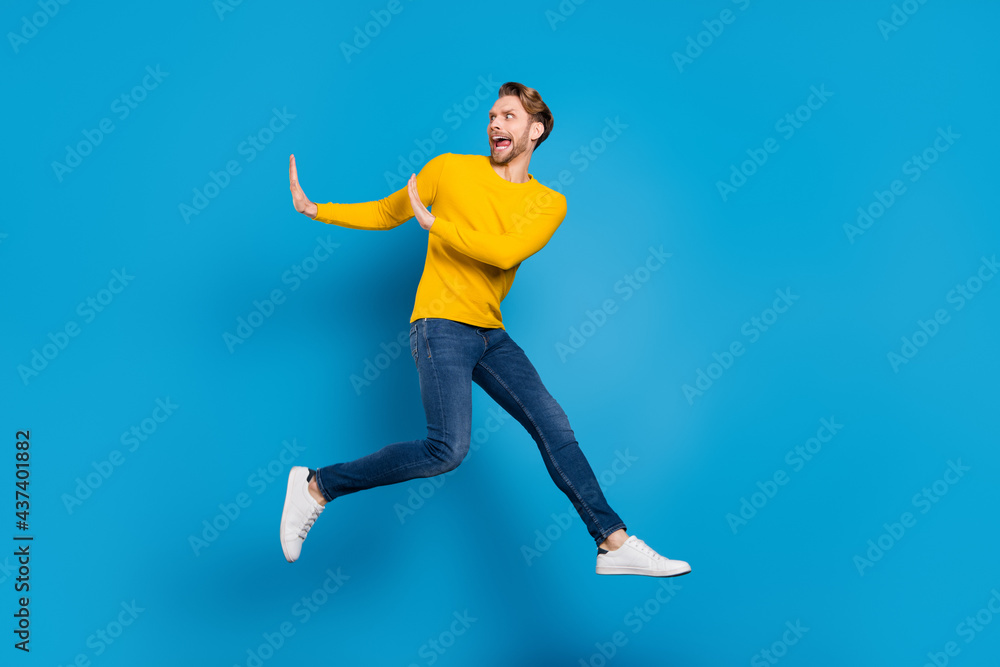 Fototapeta premium Full length body size of young guy jumping running away rejecting refusing isolated vibrant blue color background