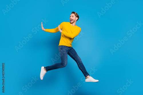 Full length body size of young guy jumping running away rejecting refusing isolated vibrant blue color background